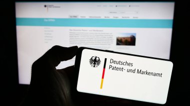 Stuttgart, Almanya - 10-17-2023: Alman Deutsches Patent-und Markenamt (DPMA) şirketinin logosuna sahip cep telefonu sahibi kişi web sayfası önünde. Telefon ekranına odaklan.