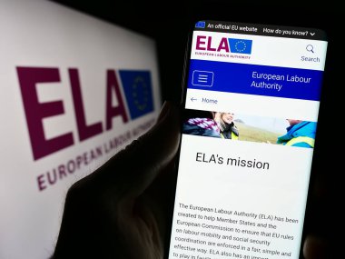 Stuttgart, Almanya - 10-20-2023: Logo önünde AB 'nin Avrupa İşçi Otoritesi (ELA) web sitesi ile akıllı telefon taşıyan kişi. Telefon ekranının merkezine odaklan.