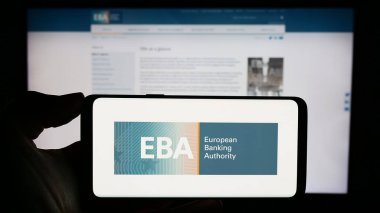 Stuttgart, Almanya - 10-20-2023: İnternet sayfası önünde AB kurumu Avrupa Bankacılık Dairesi 'nin (EBA) logosuyla cep telefonu tutan kişi. Telefon ekranına odaklan.