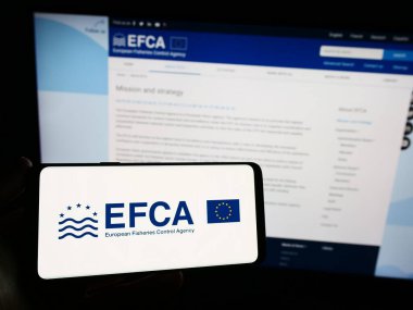 Stuttgart, Almanya - 10-20-2023: İnternet sitesi önünde AB kurumu Avrupa Balıkçılık Kontrol Dairesi (EFCA) logosuna sahip akıllı telefon sahibi kişi. Telefon ekranına odaklan.