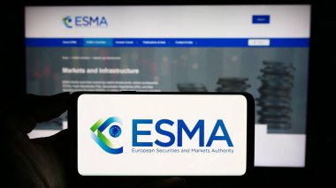 Stuttgart, Germany - 10-20-2023: Person holding cellphone with logo of European Securities and Markets Authority (ESMA) in front of webpage. Focus on phone display. clipart