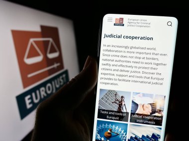 Stuttgart, Germany - 10-20-2023: Person holding smartphone with webpage of EU Agency for Criminal Justice Cooperation (Eurojust) with logo. Focus on center of phone display. clipart