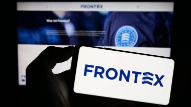 Stuttgart, Almanya - 10-25-2023: İnternet sayfası önünde Avrupa Sınır ve Sahil Güvenlik Ajansı (Frontex) logosu olan cep telefonu sahibi kişi. Telefon ekranına odaklan.