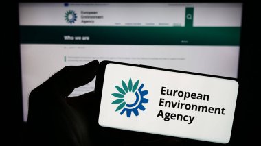 Stuttgart, Germany - 10-25-2023: Person holding mobile phone with logo of EU institution European Environment Agency (EEA) in front of web page. Focus on phone display. clipart