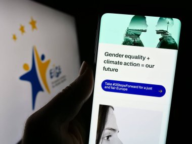 Stuttgart, Germany - 10-25-2023: Person holding smartphone with webpage of European Institute for Gender Equality (EIGE) in front of logo. Focus on center of phone display. clipart