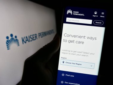 Stuttgart, Almanya - 10-27-2023: ABD yönetimindeki bakım konsorsiyumu Kaiser Permanente 'nin web sitesi ile logo önünde cep telefonu tutan kişi. Telefon ekranının merkezine odaklan.