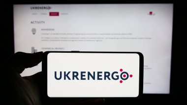 Stuttgart, Almanya - 10-27-2023: Ukraynalı ulusal enerji şirketi Ukrenergo 'nun logosuyla cep telefonu sahibi kişi iş sayfasının önünde. Telefon ekranına odaklan.
