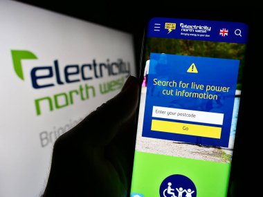 Stuttgart, Almanya - 10-28-2023: İngiliz enerji şirketi Electricity North West Limited 'in internet sayfası ile logo önünde cep telefonu tutan kişi. Telefon ekranının merkezine odaklan.