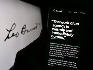 Stuttgart, Almanya - 10-28-2023: ABD 'li reklam şirketi Leo Burnett Worldwide Inc.' in internet sayfası ile logo önünde cep telefonu tutan kişi. Telefon ekranının merkezine odaklan.