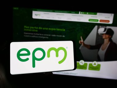 Stuttgart, Almanya - 10-29-2023: İnternet sayfası önünde Kolombiyalı Empresas Publicas de Medellin (EPM) şirketinin logosu olan cep telefonu sahibi kişi. Telefon ekranına odaklan.