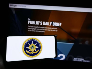 Stuttgart, Almanya - 10-29-2023: İnternet sayfası önünde ABD İstihbarat Topluluğu (IC) örgütünün mührü altında cep telefonu tutan kişi. Telefon ekranına odaklan.