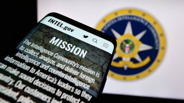 Stuttgart, Germany - 10-29-2023: Mobile phone with website of agency group United States Intelligence Community (IC) in front of seal. Focus on top-left of phone display. clipart