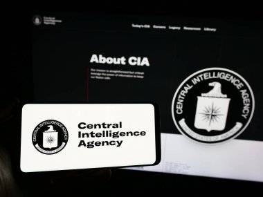 Stuttgart, Germany - 10-29-2023: Person holding mobile phone with logo of American Central Intelligence Agency (CIA) in front of web page. Focus on phone display. clipart