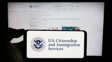 Stuttgart, Almanya - 10-29-2023: İnternet sayfası önünde ABD vatandaşlık ve Göçmenlik Hizmetleri (USCIS) mührü bulunan cep telefonu sahibi kişi. Telefon ekranına odaklan.