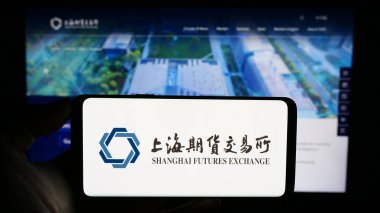 Stuttgart, Germany - 10-30-2023: Person holding cellphone with logo of Chinese Shanghai Futures Exchange (ShFE) in front of company webpage. Focus on phone display. clipart