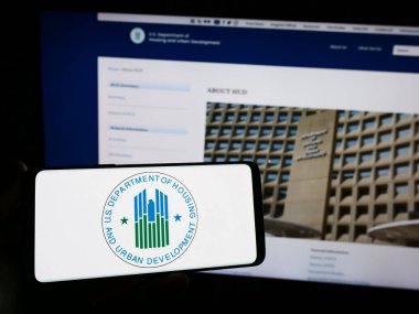Stuttgart, Almanya - 10-30-2023: İnternet sitesi önünde ABD Konut ve Kentsel Kalkınma Dairesi (İmar ve Kalkınma Bakanlığı) logosu olan akıllı telefon sahibi kişi. Telefon ekranına odaklan.