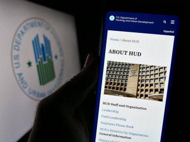 Stuttgart, Almanya - 10-30-2023: ABD Konut ve Kentsel Gelişim Bakanlığı (İmar ve Kalkınma Bakanlığı) web sayfası logonun önünde cep telefonu tutan kişi. Telefon ekranının merkezine odaklan.