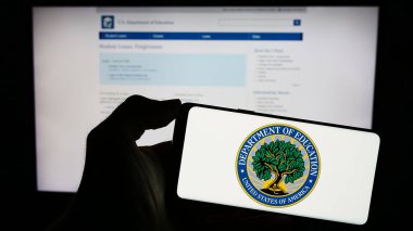 Stuttgart, Almanya - 10-30-2023: ABD Eğitim Bakanlığı mührü ile cep telefonunu web sayfası önünde tutan kişi. Telefon ekranına odaklan.