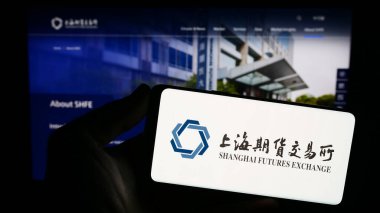 Stuttgart, Germany - 10-30-2023: Person holding smartphone with logo of Chinese Shanghai Futures Exchange (ShFE) in front of website. Focus on phone display. clipart