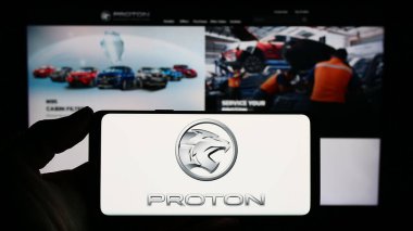 Stuttgart, Almanya - 10-31-2023: Malezyalı otomotiv şirketi Proton Holding Berhad 'ın (PHB) logosuna sahip akıllı telefon sahibi kişi web sitesi önünde. Telefon ekranına odaklan.