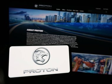 Stuttgart, Germany - 10-31-2023: Person holding mobile phone with logo of Malaysian automotive company Proton Holdings Berhad (PHB) in front of web page. Focus on phone display. clipart