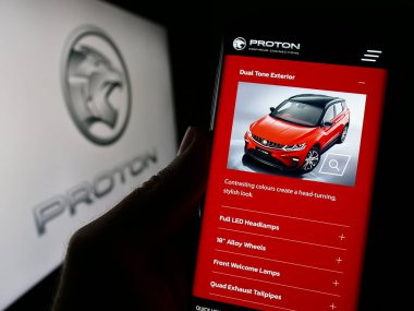 Stuttgart, Almanya - 10-31-2023: Malezyalı otomotiv şirketi Proton Holding Berhad 'ın (PHB) logolu web sayfası ile cep telefonu tutan kişi. Telefon ekranının merkezine odaklan.
