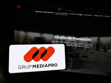 Stuttgart, Germany - 10-31-2023: Person holding smartphone with logo of Spanish multimedia company Mediapro Group in front of website. Focus on phone display. clipart