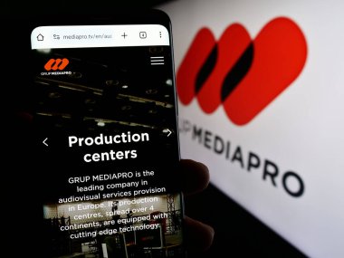 Stuttgart, Almanya - 10-31-2023: İspanyol multimedya şirketi Mediapro Group 'un web sayfası ile iş logosu önünde cep telefonu tutan kişi. Telefon ekranının merkezine odaklan.