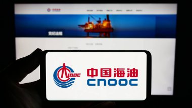 Stuttgart, Almanya - 09-10-2023: İnternet sitesi önünde üzerinde Çin Ulusal Offshore Oil Corporation (CNOOC) logosu bulunan akıllı telefon sahibi kişi. Telefon ekranına odaklan.