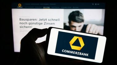 Stuttgart, Almanya - 09-10-2023: Alman finans şirketi Commerzbank AG 'nin logosuyla cep telefonu sahibi kişi iş sayfasının önünde ekranda. Telefon ekranına odaklan.