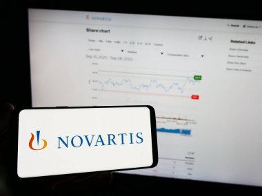 Stuttgart, Almanya - 09-10-2023: İsviçreli ilaç şirketi Novartis AG 'nin logosuna sahip cep telefonu sahibi kişi iş sayfasının önünde ekranda görülüyor. Telefon ekranına odaklan.