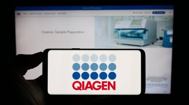 Stuttgart, Germany - 09-10-2023: Person holding cellphone with logo of biotechnology company Qiagen N.V. on screen in front of business webpage. Focus on phone display. clipart