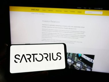 Stuttgart, Almanya - 09-10-2023: Alman ilaç firması Sartorius AG 'nin logosunu elinde tutan kişi web sitesinin önünde ekranda. Telefon ekranına odaklan.