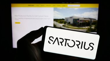 Stuttgart, Almanya - 09-10-2023: Alman ilaç şirketi Sartorius AG 'nin logosunun bulunduğu cep telefonu sahibi kişi iş sayfasının önünde ekranda. Telefon ekranına odaklan.