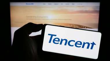 Stuttgart, Almanya - 09-11-2023: Çinli şirket Tencent Holding Ltd. 'nin logosuyla cep telefonu sahibi kişi iş sayfasının önünde ekranda. Telefon ekranına odaklan.