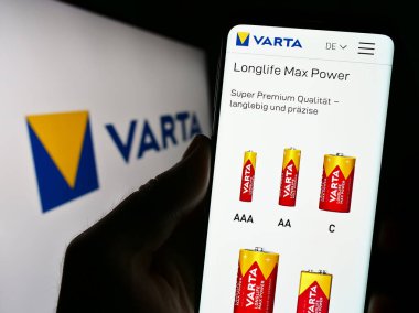 Stuttgart, Germany - 09-11-2023: Person holding cellphone with webpage of German battery company Varta AG on screen in front of business logo. Focus on center of phone display. clipart