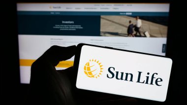 Stuttgart, Almanya - 09-14-2023: Kanadalı Sun Life Financial Inc. şirketinin logosuyla cep telefonu sahibi kişi iş sayfasının önünde ekranda. Telefon ekranına odaklan.
