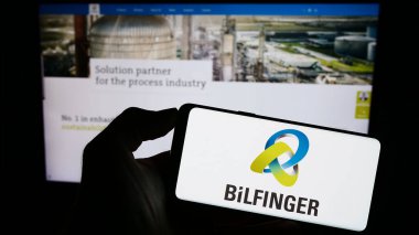 Stuttgart, Almanya - 09-14-2023: Alman inşaat şirketi Bilfinger SE 'nin logosuyla cep telefonu sahibi kişi iş sayfasının önünde ekranda. Telefon ekranına odaklan.