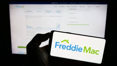 Stuttgart, Almanya - 09-17-2023: Amerikan ipotek şirketi Freddie Mac 'in logosunun bulunduğu cep telefonu sahibi kişi iş sayfasının önünde ekranda. Telefon ekranına odaklan.
