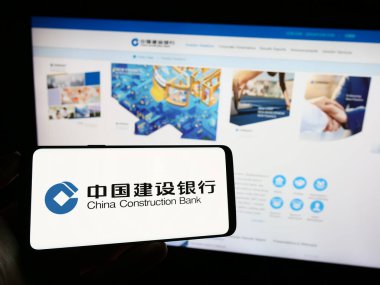 Stuttgart, Almanya - 09-17-2023: Çin İnşaat Bankası Şirketi 'nin (CCB) logosuna sahip cep telefonu sahibi kişi web sayfası önünde ekranda. Telefon ekranına odaklan.