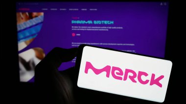 Stuttgart, Almanya - 09-17-2023: Alman ilaç şirketi Merck KGaA 'nın logosunun bulunduğu cep telefonu sahibi kişi iş sayfasının önünde ekranda. Telefon ekranına odaklan.