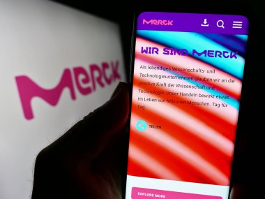 Stuttgart, Almanya - 09-17-2023: Alman ilaç firması Merck KGaA 'nın internet sitesi ile cep telefonu tutan kişi logonun önünde ekranda. Telefon ekranının merkezine odaklan.