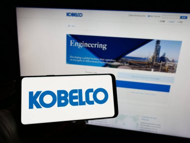Stuttgart, Almanya - 09-17-2023: Japon şirketi Kobe Steel Ltd. (Kobelco) 'nun logosuyla cep telefonu sahibi kişi iş sayfasının önünde ekranda. Telefon ekranına odaklan.