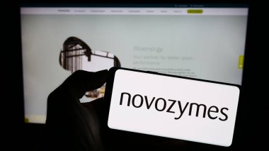 Stuttgart, Almanya - 09-17-2023: Danimarkalı biyoteknoloji şirketi Novozymes AS 'in logosuyla cep telefonu sahibi kişi iş sayfasının önünde ekranda görülüyor. Telefon ekranına odaklan.