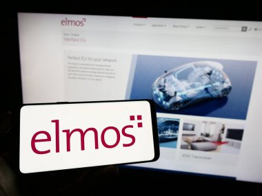 Stuttgart, Almanya - 09-17-2023: Alman şirketi Elmos Semiconductor SE 'nin logosuyla cep telefonu sahibi kişi iş sayfasının önünde ekranda. Telefon ekranına odaklan.