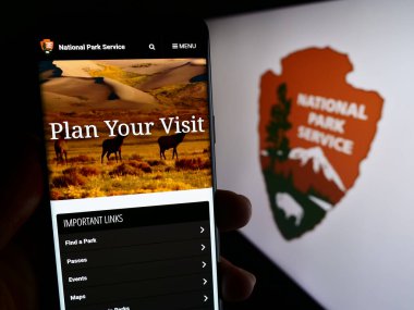 Stuttgart, Almanya - 09-17-2023: ABD 'nin Ulusal Park Hizmetleri (NPS) sitesinin internet sayfası logonun önünde cep telefonu tutan kişi. Telefon ekranının merkezine odaklan.