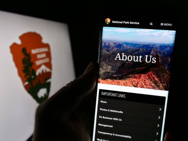 Stuttgart, Almanya - 09-17-2023: ABD 'nin Ulusal Park Hizmetleri (NPS) sitesinin logo önünde cep telefonu tutan kişi. Telefon ekranının merkezine odaklan.