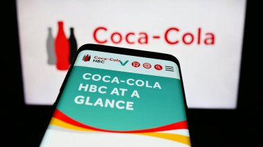 Stuttgart, Germany - 09-18-2023: Smartphone with webpage of beverage company Coca-Cola HBC AG on screen in front of business logo. Focus on top-left of phone display. clipart