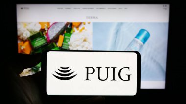 Stuttgart, Almanya - 09-18-2023: İspanyol modası ve parfüm şirketi Puig S.L. logosuna sahip cep telefonu sahibi kişi Web sayfasının önünde ekranda. Telefon ekranına odaklan.