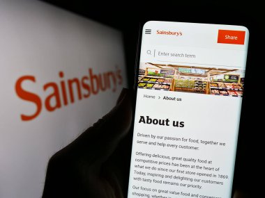 Stuttgart, Almanya - 09-19-2023: İngiliz süpermarket şirketi J Sainsbury plc 'in web sitesi olan cep telefonu logosu önünde ekranda. Telefon ekranının merkezine odaklan.